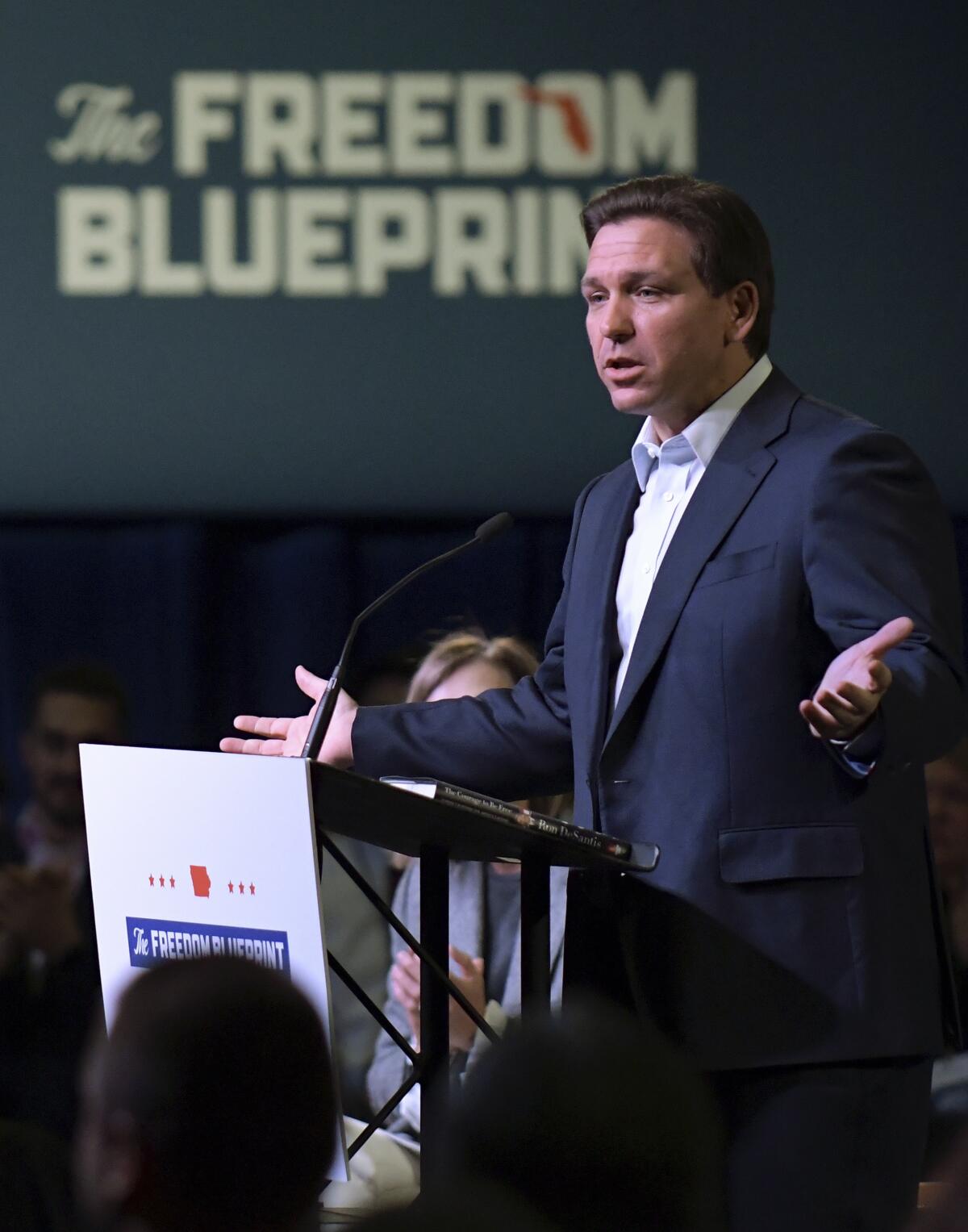 A man in a suit speaks into a microphone at a podium 