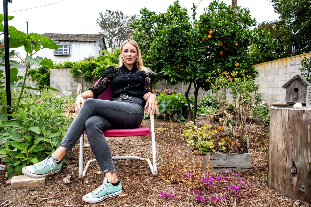 A woman sits in a chair surrounded by different types of plants and mulch