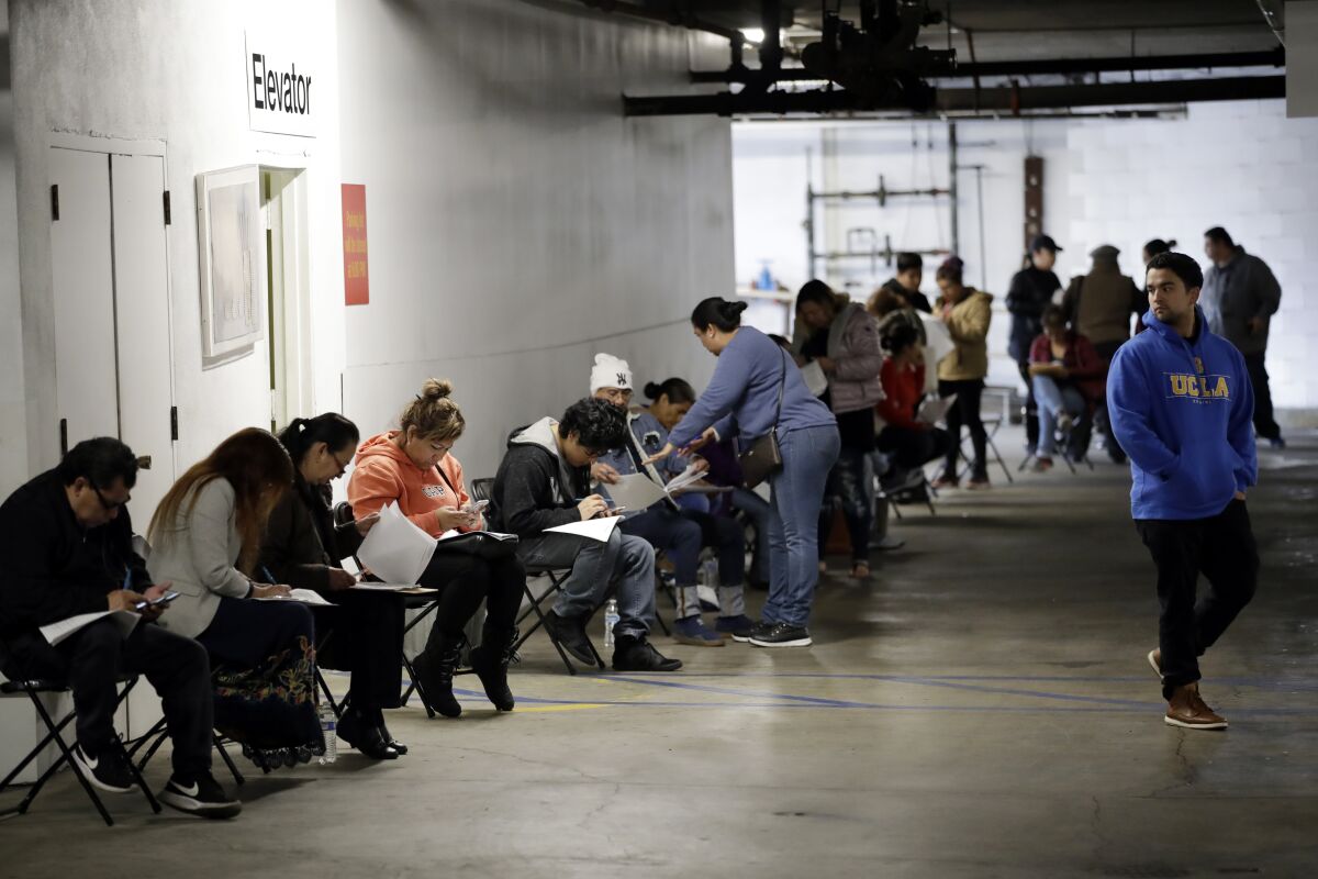 Hospitality workers wait in line in a basement garage to apply for unemployment benefits