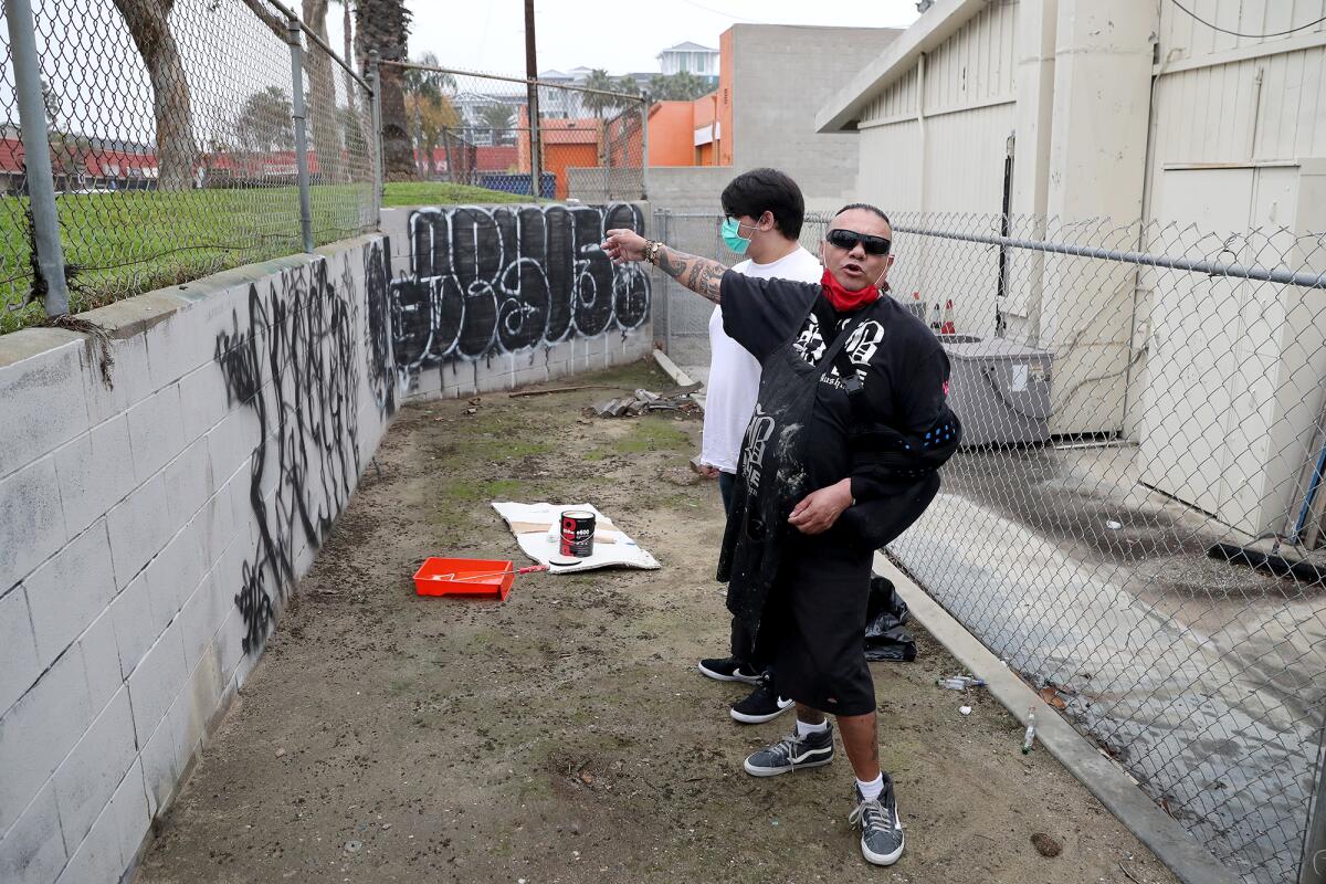 Adam "Bushman" Orozco, 59, right, and his son Thunder, 22, left, clean up graffiti Friday in Huntington Beach.