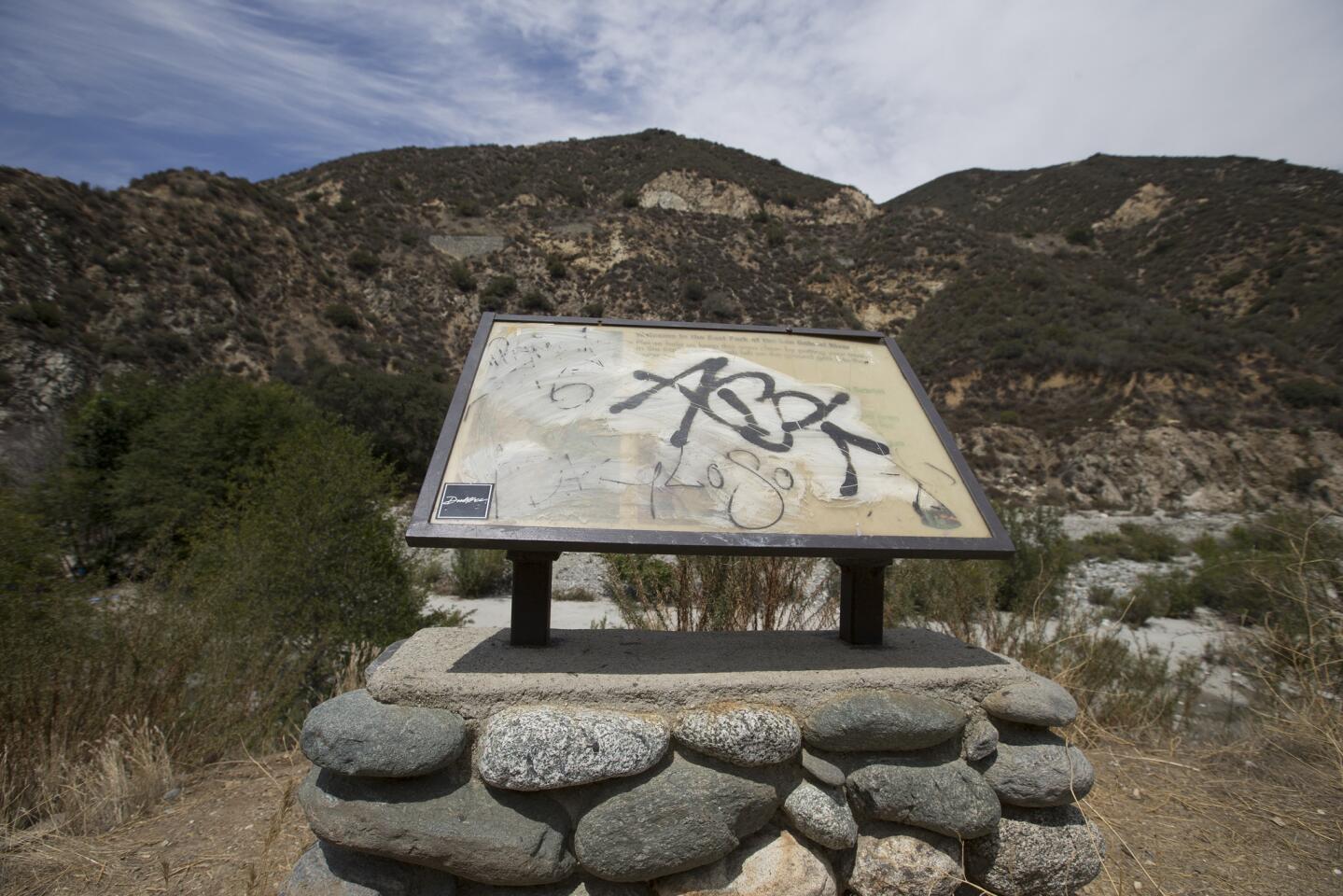 A grafitti-covered sign provides information about the national monument and asks visitors to remove their trash.