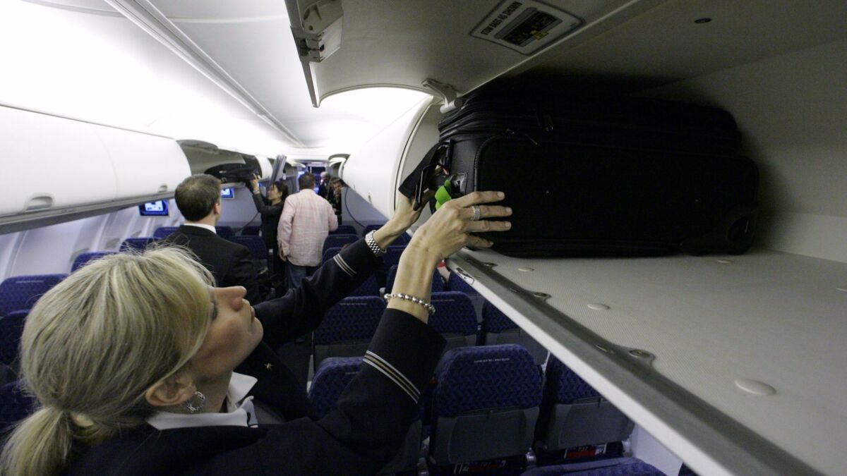 American Airlines flight attendant Renee Schexnaildre demonstrates the overhead baggage area during a media preview of a Boeing 737-800 jet. Flight attendants say bulky carry-on bags cause them injuries.