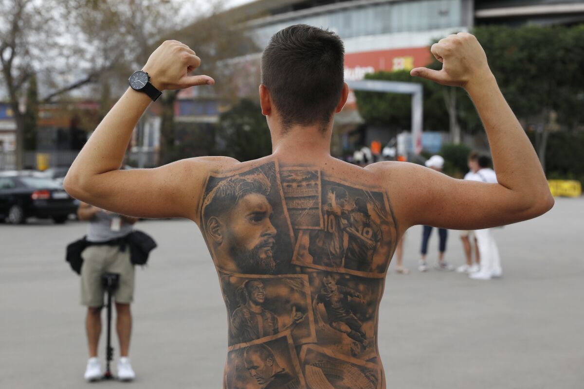 FILE - In this Friday, Aug. 6, 2021 file photo, a Barcelona fan poses showing tattoos of Lionel Messi and other Barcelona players before FC Barcelona club President Joan Laporta gives a news conference in Barcelona, Spain. Barcelona’s first season without Lionel Messi after nearly two decades starts with a home match against Real Sociedad on Sunday Aug. 15, 2021. The fans are still adjusting to the loss of the club's greatest player. Messi signed a two-year contract with Paris Saint-Germain. (AP Photo/Joan Monfort, File)