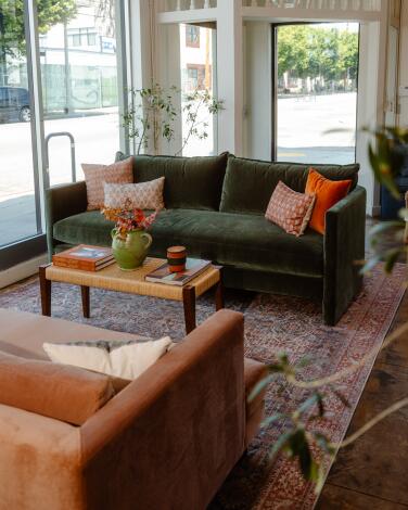 A green sofa and orange sofa face each other with a wood coffee table in the center in Clad Home's showroom.