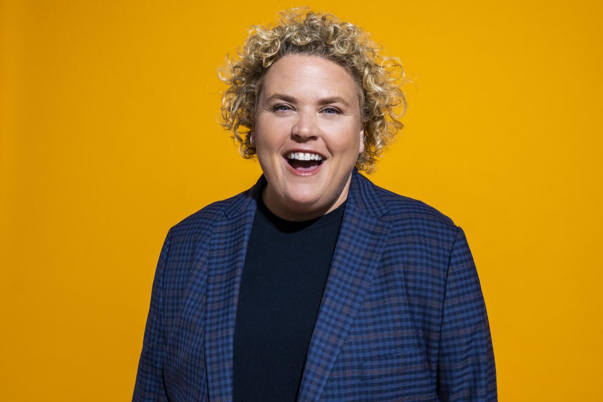 Woman with short blond curly hair smiling in front of yellow background