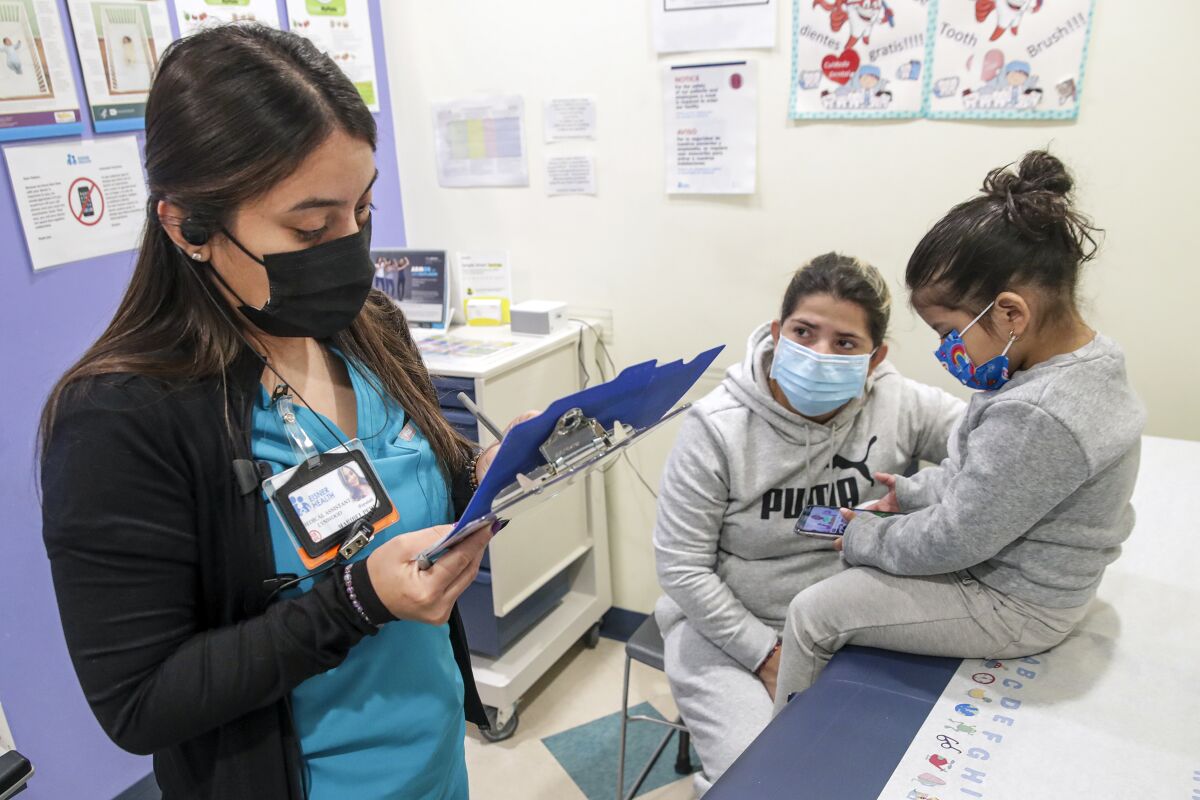 A child sits atop a medical exam table while a medical assistant takes notes