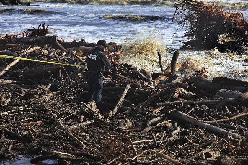 A Capitola police officer tapes off dangerous areas of driftwood along Capitola Beach as strong waves continue to batter the central California coast in Capitola, Calif., Tuesday, Jan. 10, 2023. (Shmuel Thaler/The Santa Cruz Sentinel via AP)