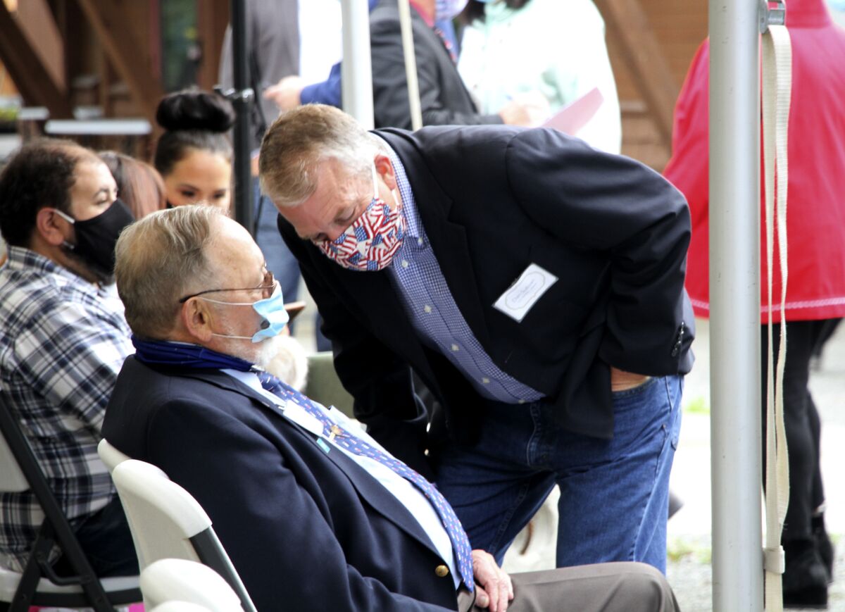 A masked U.S. Sen. Daniel Sullivan leans down to speak to a seated U.S. Rep. Don Young, also masked.