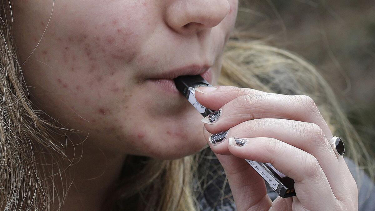 A high school student uses a vaping device near a school campus in Cambridge, Mass., on April 11, 2018.