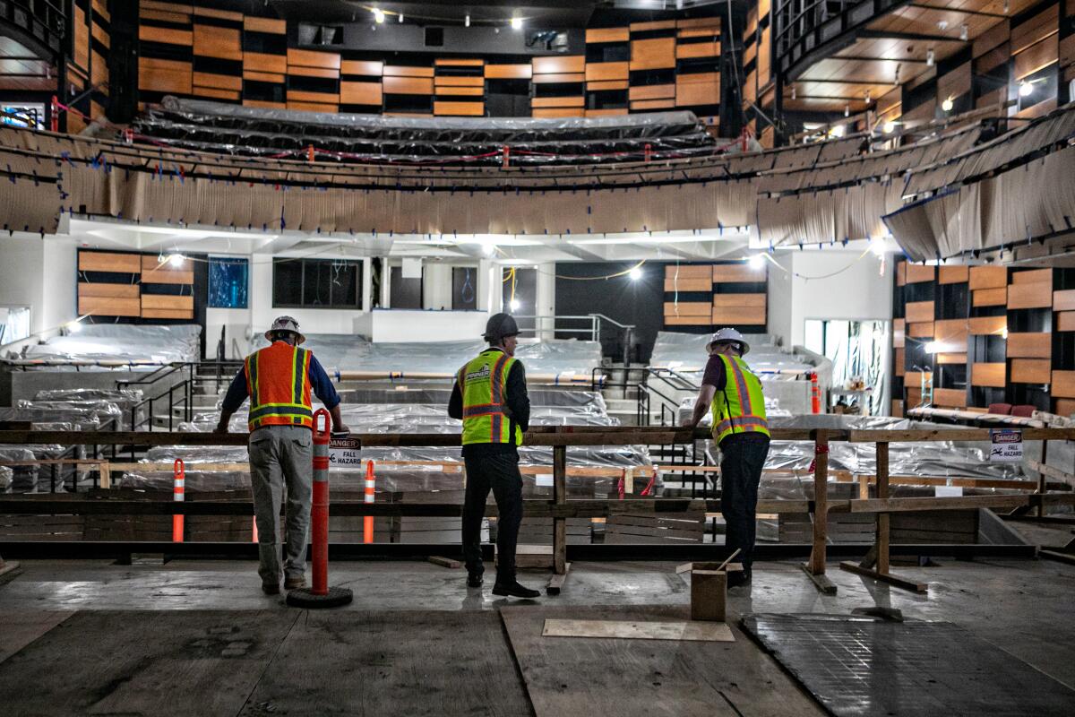 Three people in yellow or orange safety vests in a theater under construction.