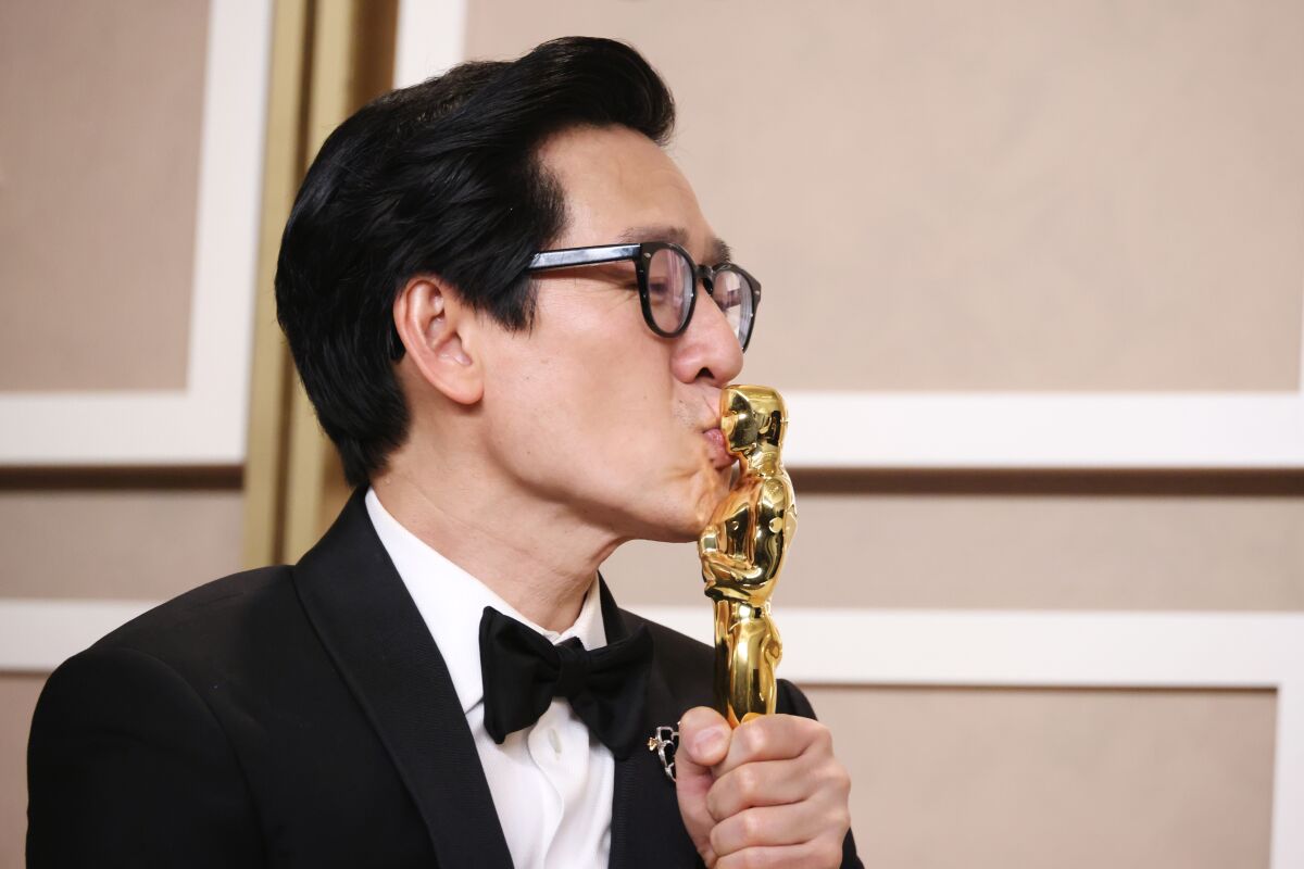A man in a tuxedo kisses an Oscar statuette.  