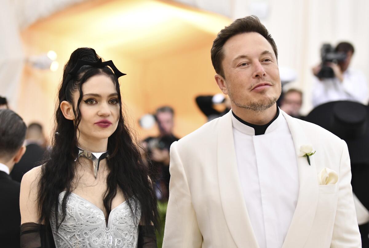 Grimes wears a silver dress and Elon Musk a white suit as the two pose for photos at the Met Gala