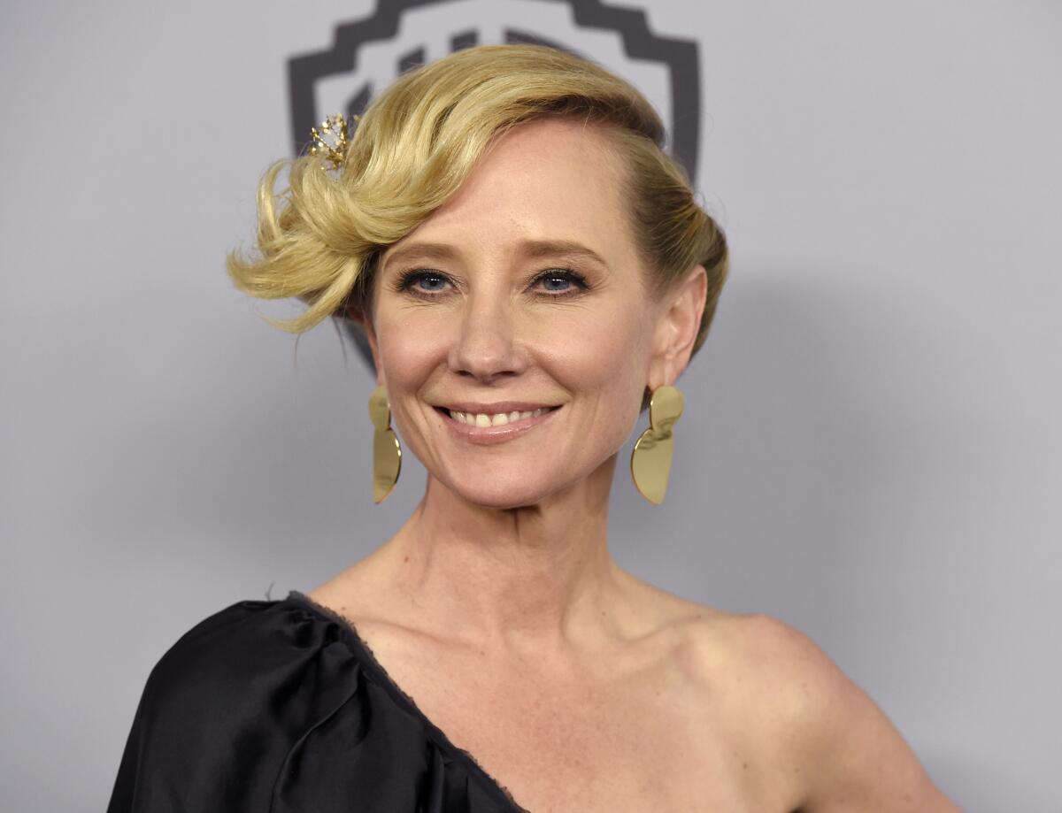 Anne Heche posing in gold earrings and a one-shoulder black dress