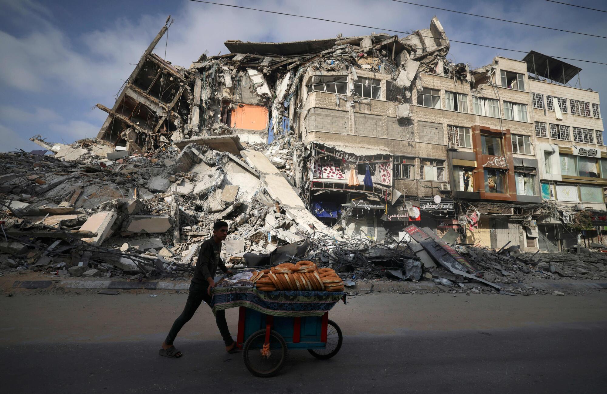 A man pushes a cart past a wrecked building