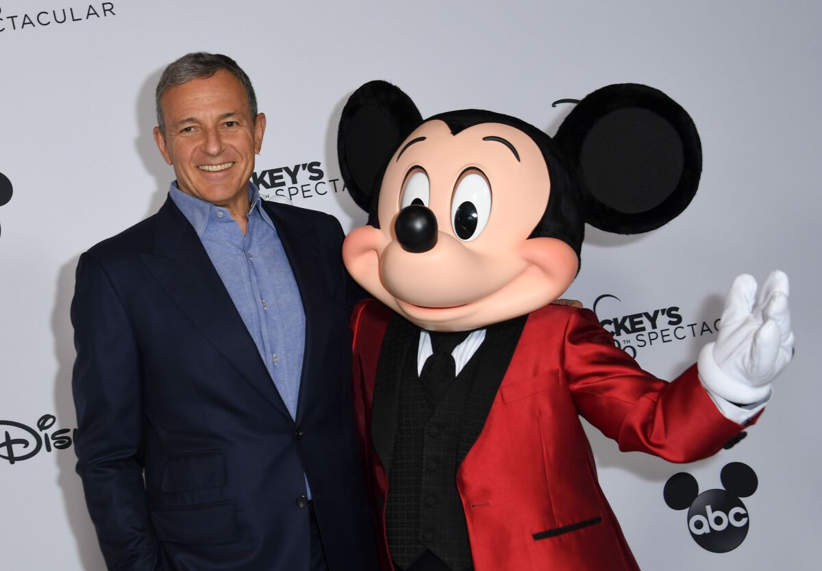 Bob Iger in a suit stands next to Mickey Mouse.