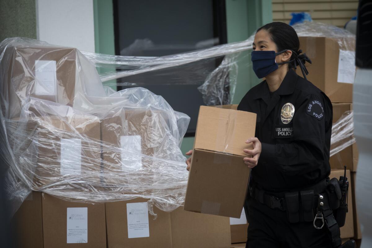 LAPD Officer Kat Piamonte carries a box of supplies during food distribution effort in Hollywood on Thursday.