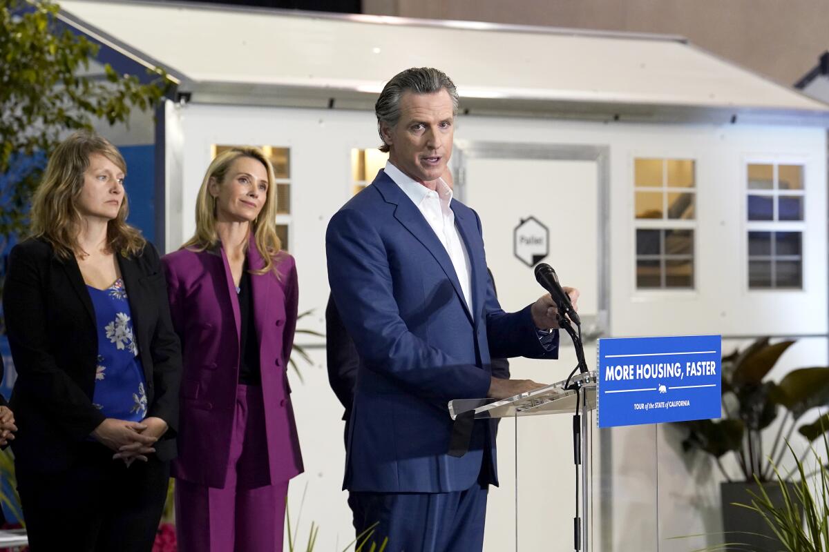 Gov. Gavin Newsom speaking at a lectern as two people look on