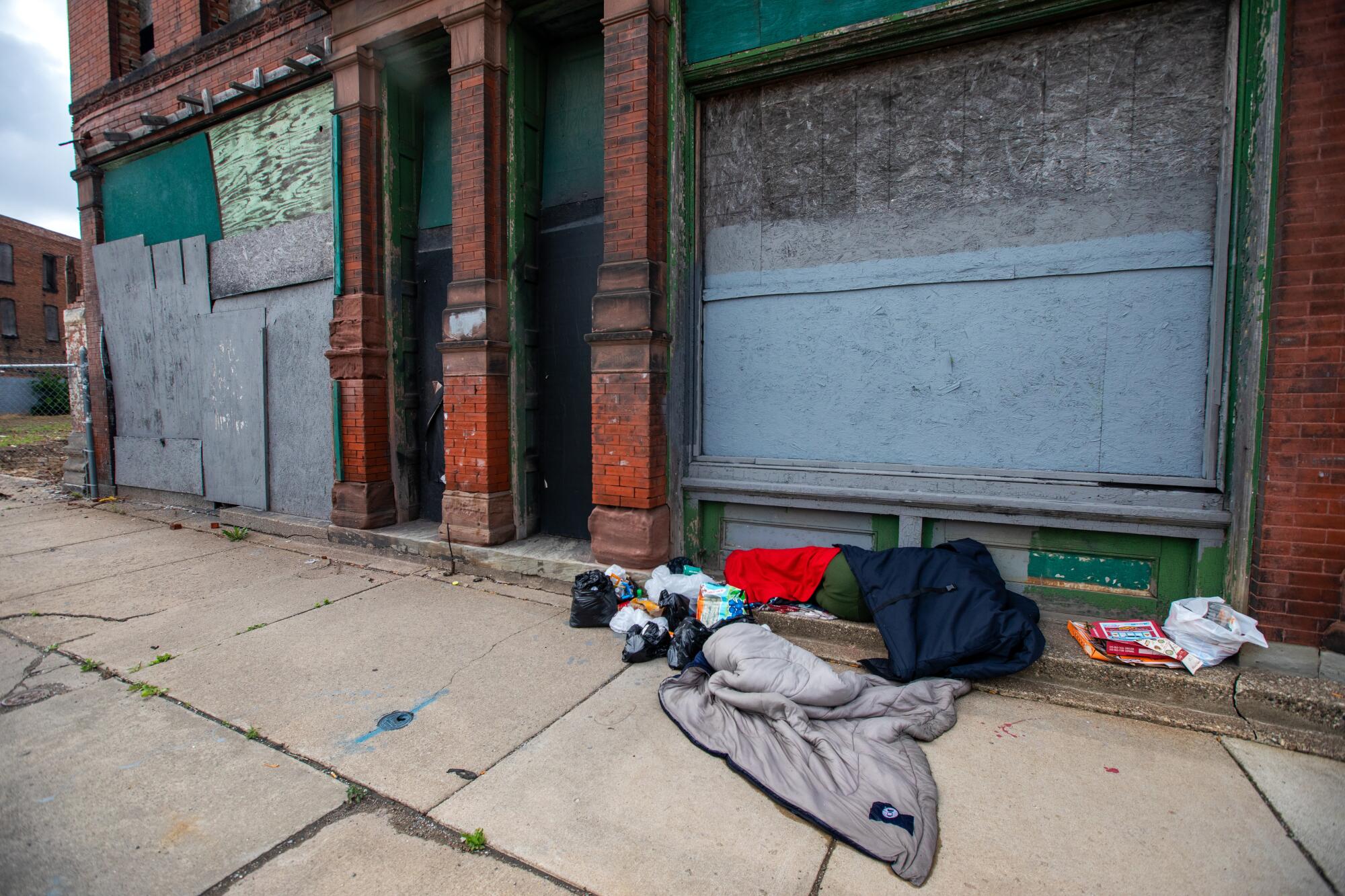 A person sleeps under a coat in front of an abandoned building in Detroit.