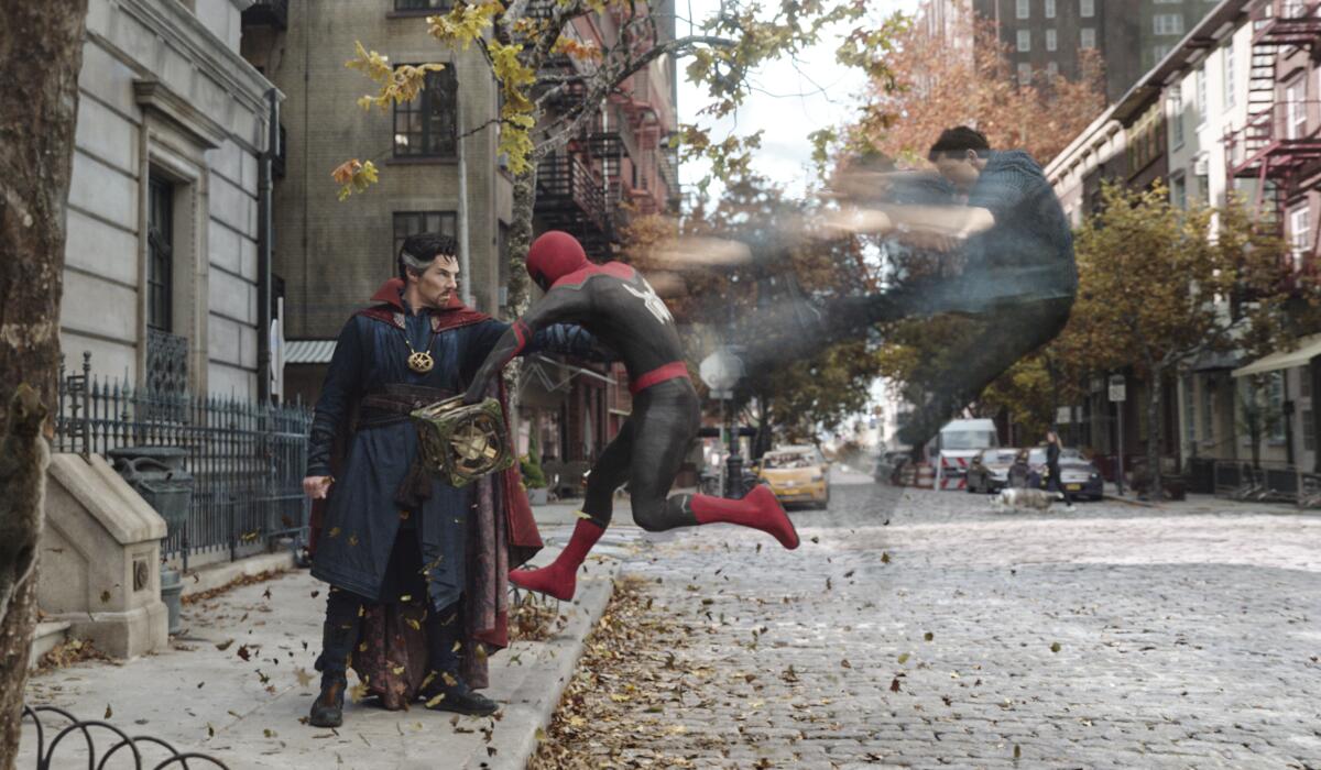 A man wearing a cape and standing on a sidewalk hits a man in a Spider-Man suit