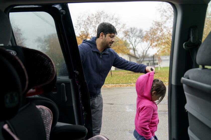 A man pulls up the hood of a girl's pink jacket near a vehicle