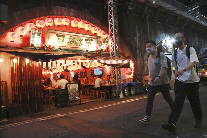 Masked men walk past a brightly lit restaurant on a Tokyo street