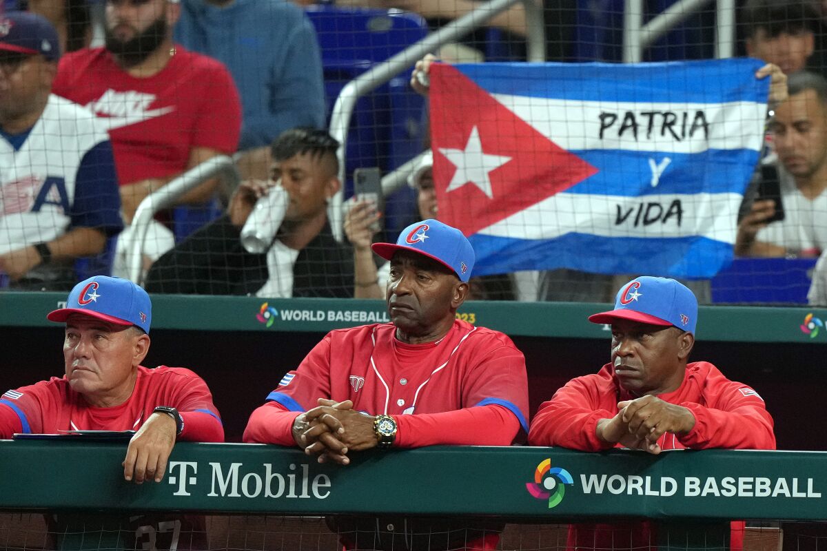 Cuba manager Armando Johnson looks on from the dugout as fans hold a Cuban flag displaying the words "Patria y Vida” on it.