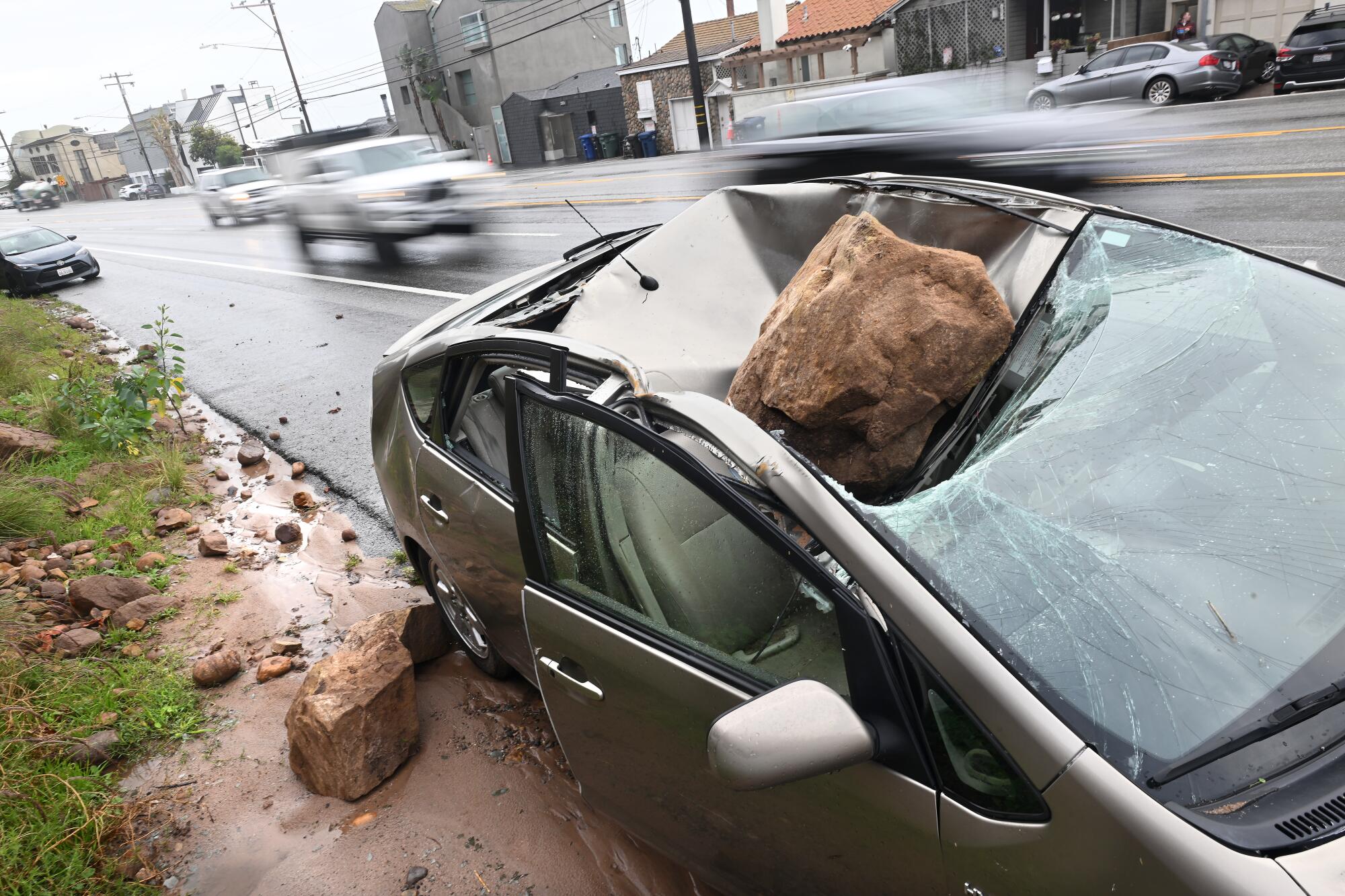 A boulder sits on a car it damaged.