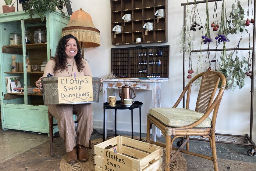 A woman sitting down on a chair holding a bin with a sign that says "clothes swap donations."