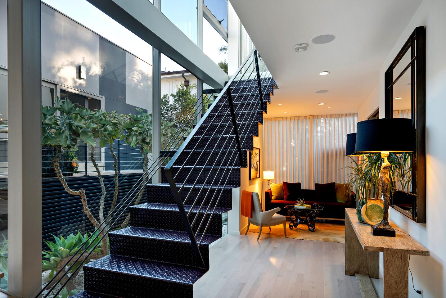 Stairs leading up next to glass walls and a furnished room down the hall.