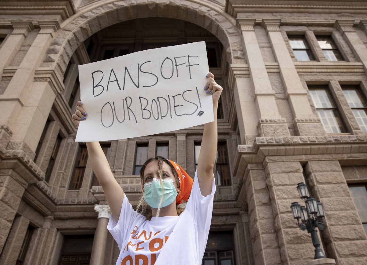 A woman in a mask holds up a sign that says Bans off our bodies!