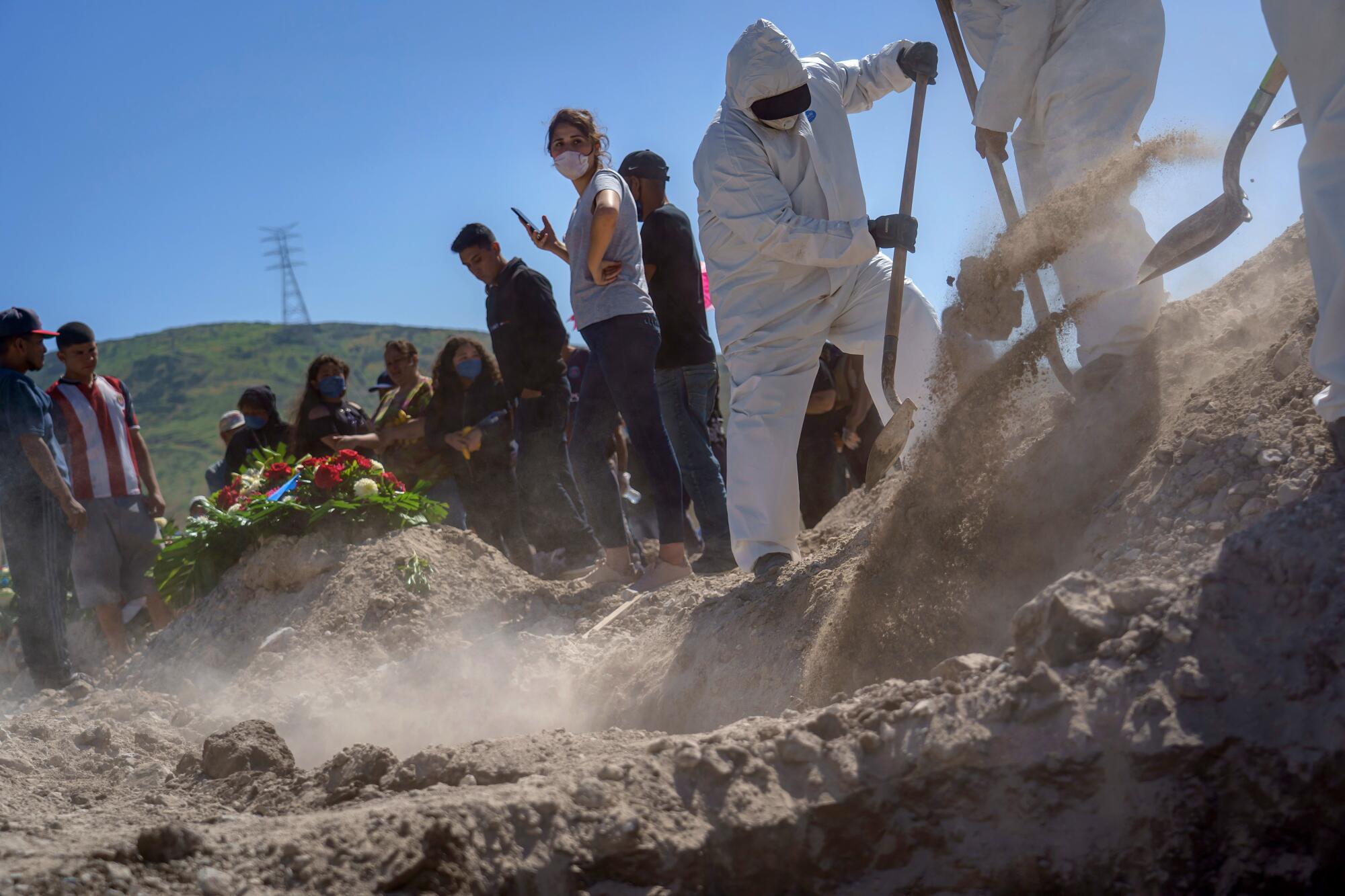 Family members watch as gravediggers in protective suits move from burial to burial at Tijuana's Municipal Cemetery No. 13.