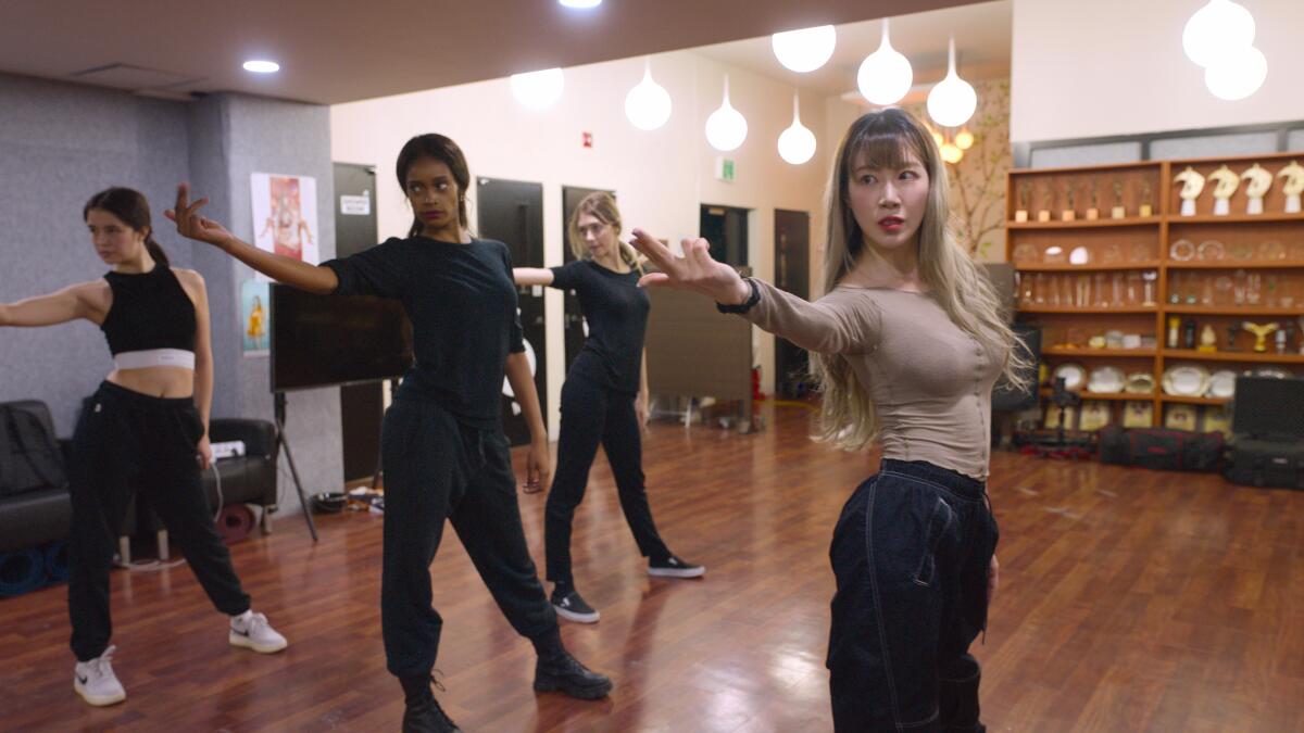 Four people in a studio or gym stretch their right arm out to the side.