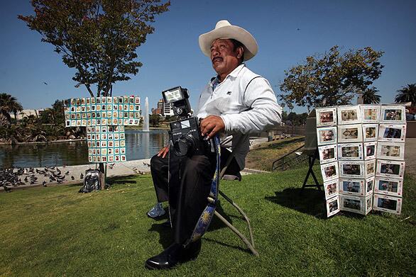 Javier Prado sits in his folding chair waiting for customers at MacArthur Park. Photographers such as Prado, with their old-fashioned Polaroid cameras, have been fixtures in the area for nearly 40 years. See full story