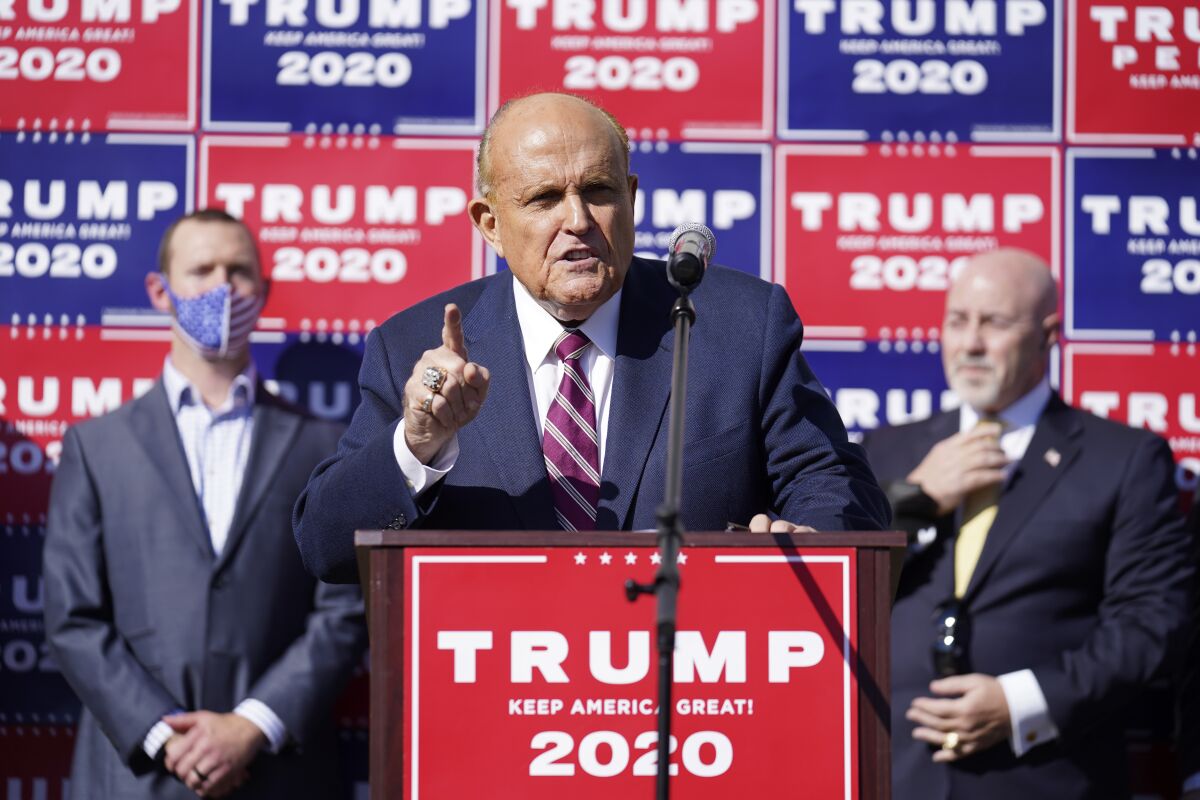 Rudy Giuliani gestures with a finger as he speaks at a lectern with a red Trump 2020 sign