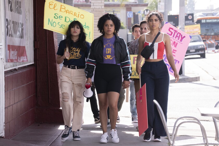 Three women carrying signs and megaphones lead a protest.
