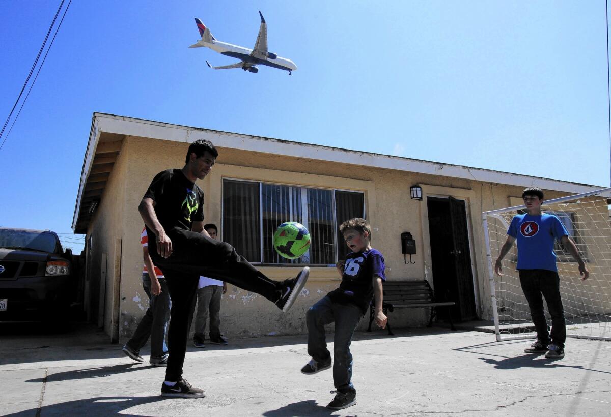A plane flies overhead as Joe Mejia, 21, left; Derick Montes, 6; and Leonardo Armenia, 14, play in Lennox. A new study has found high levels of potentially harmful particles in communities up to 10 miles east of LAX.