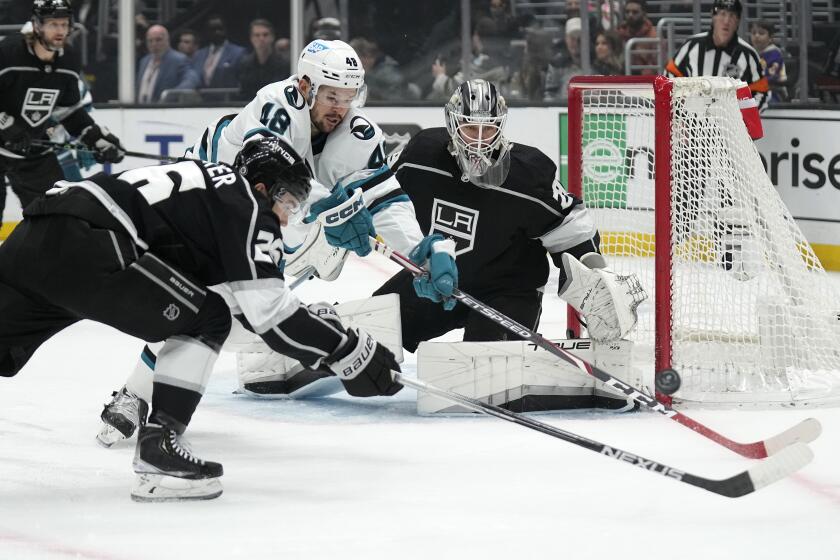 Los Angeles Kings defenseman Sean Walker, left, and San Jose Sharks center Tomas Hertl, center, reach for the puck as goaltender Pheonix Copley watches during the first period of an NHL hockey game Wednesday, Jan. 11, 2023, in Los Angeles. (AP Photo/Mark J. Terrill)