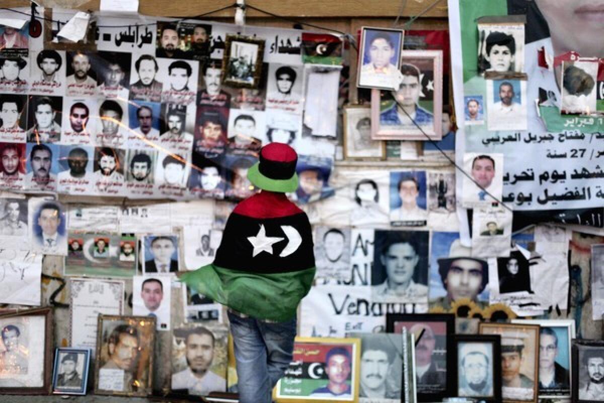 A girl wrapped in a flag looks at pictures of people killed in Libya. (Altaf Qadri / Associated Press)