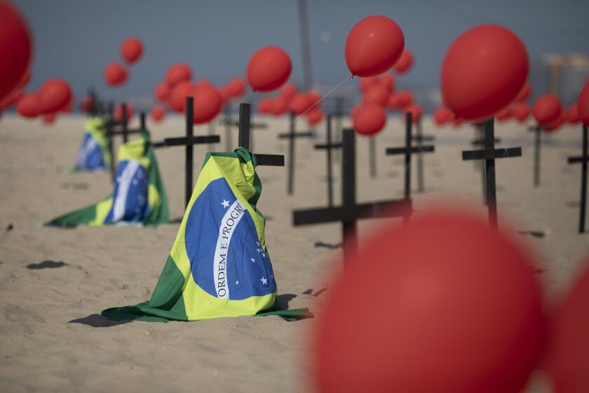 Crosses, red balloons and Brazilian nation flags are placed in the sand on Copacabana beach in a demonstration organized by Rio de Paz to honor the victims of COVID-19, as the country heads to a milestone of 100,000 new coronavirus related deaths, in Rio de Janeiro, Brazil, Saturday, Aug. 8, 2020. (AP Photo/Mario Lobao)