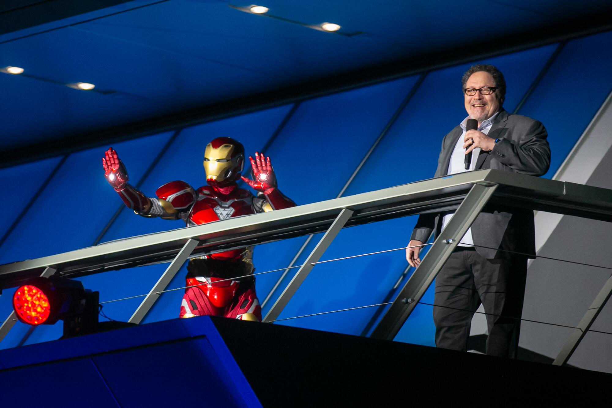 Iron Man holds up his hands onstage as Jon Favreau speaks.