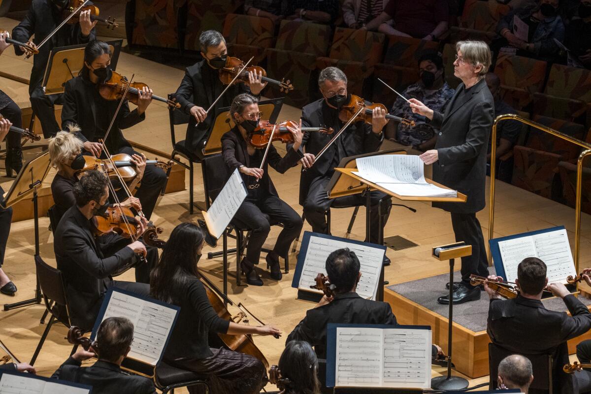 A conductor holds a baton in front seated musicians playing instruments.