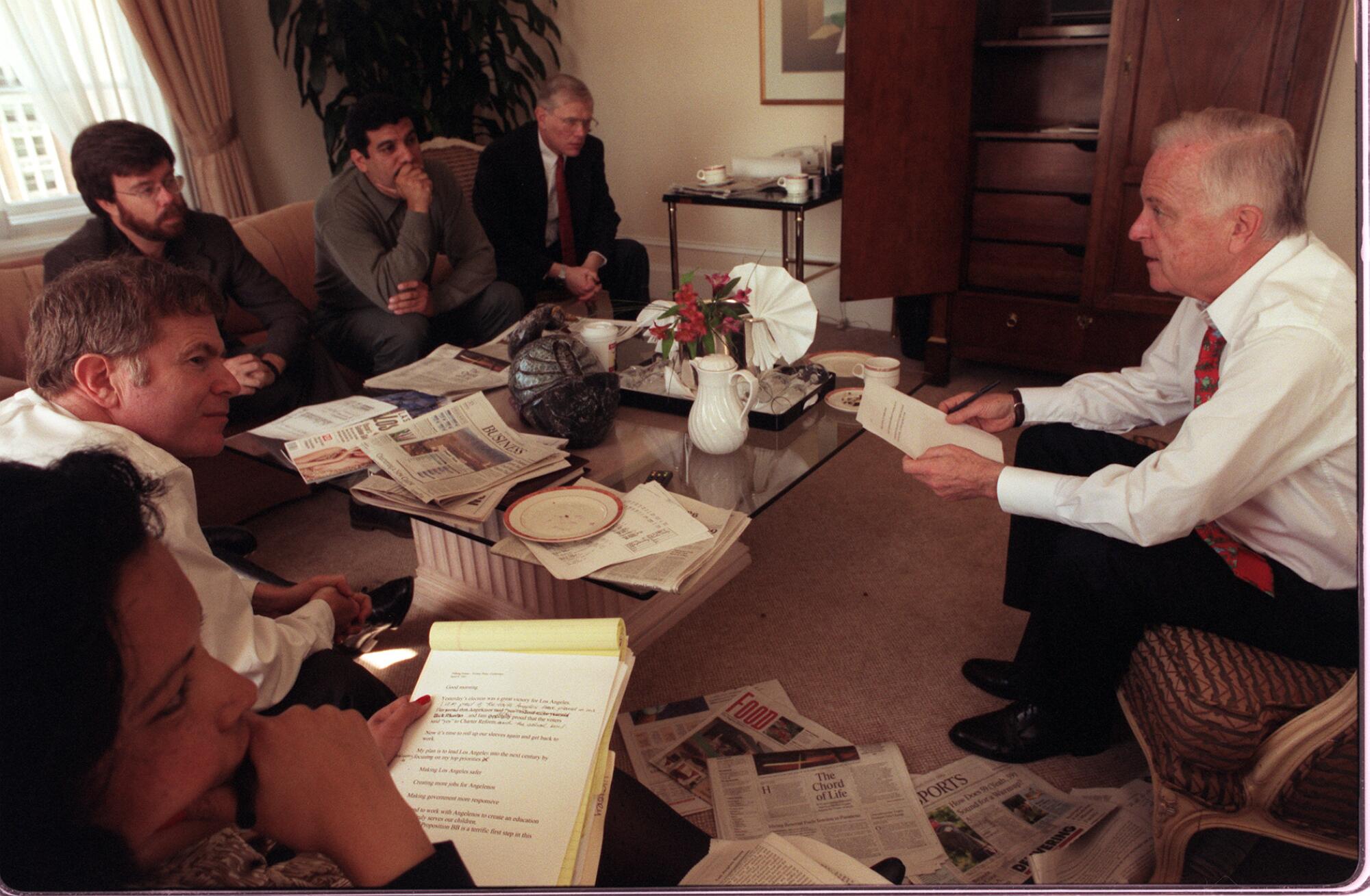 Richard Riordan leads a meeting with several staffers sitting around a coffee table strewn with papers 