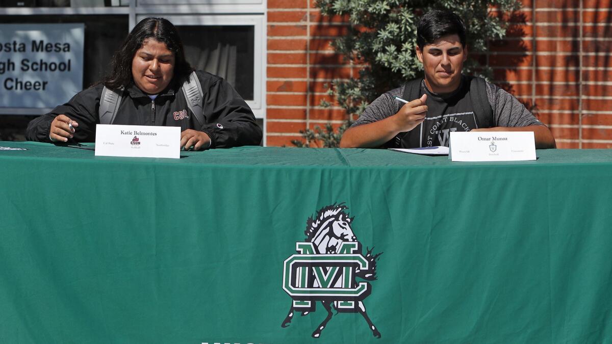 Softball player Katie Belmontes and baseball player Omar Munoz sign their letters of intent at a National Signing Day ceremony at Costa Mesa High School on Wednesday. Belmontes is headed to Cal State Northridge, and Munoz to Westcliff University.