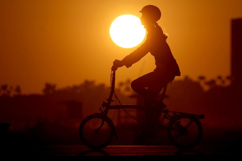 LONG BEACH, CALIF. - AUG. 11, 2022.. The sun sets as a woman pedals down the bike path in Long Beach. (Luis Sinco / Los Angeles Timesd)