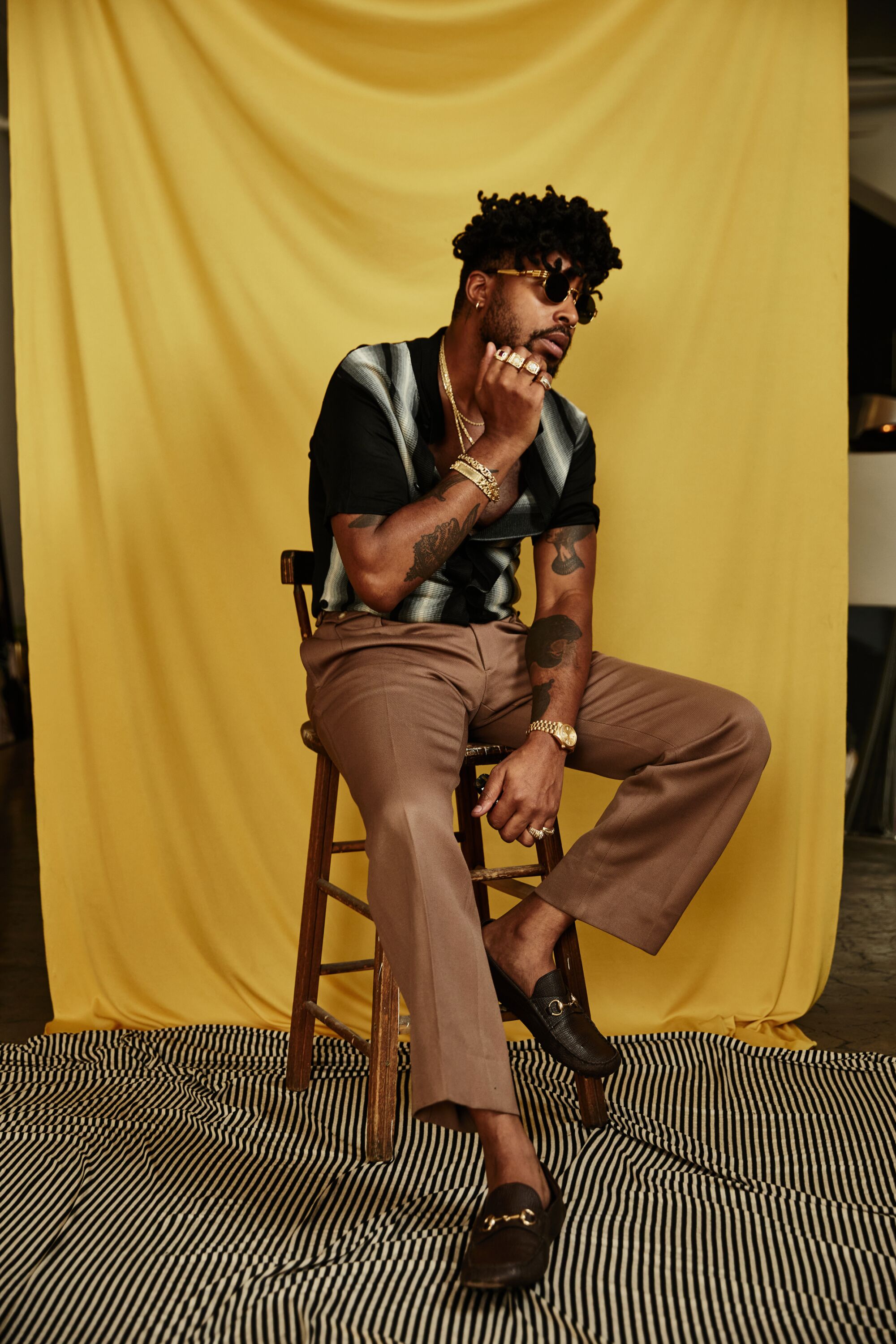 A man seated on a high chair in front of a yellow fabric backdrop.