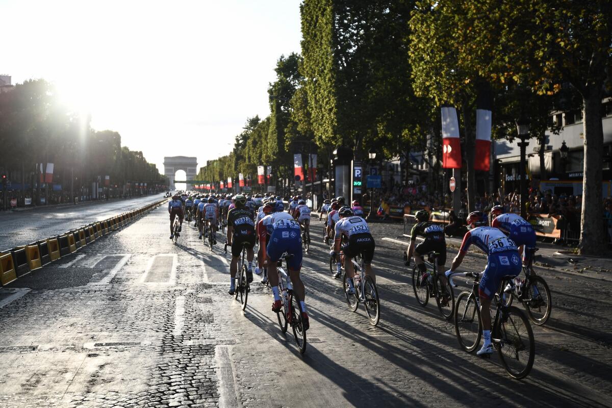 Cyclists ride down the Champs Elysees in Paris with the Arc de Triomphe ahead of them.