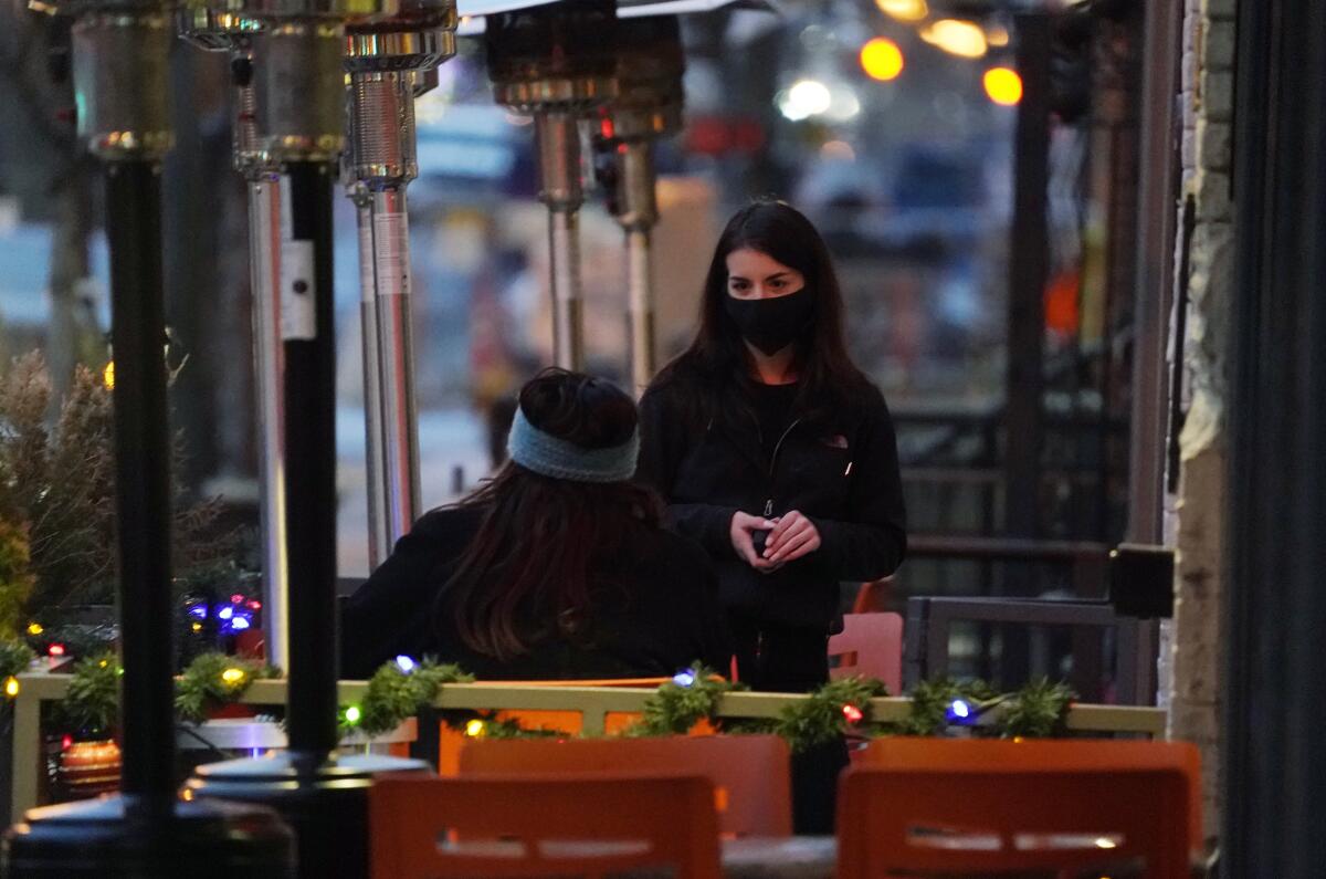 A server wears a protective mask while tending to a patron sitting in the outdoor patio of a restaurant.