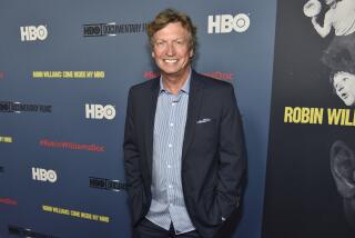 Nigel Lythgoe smiles and poses while wearing a dark blue suit jacket and a light blue dress shirt