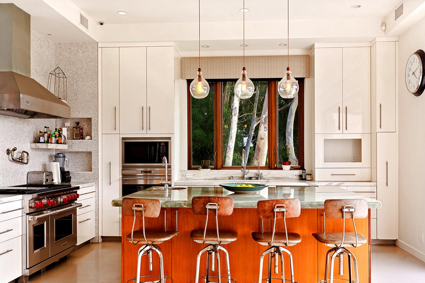 A kitchen with appliances and an island and chairs in front of it.