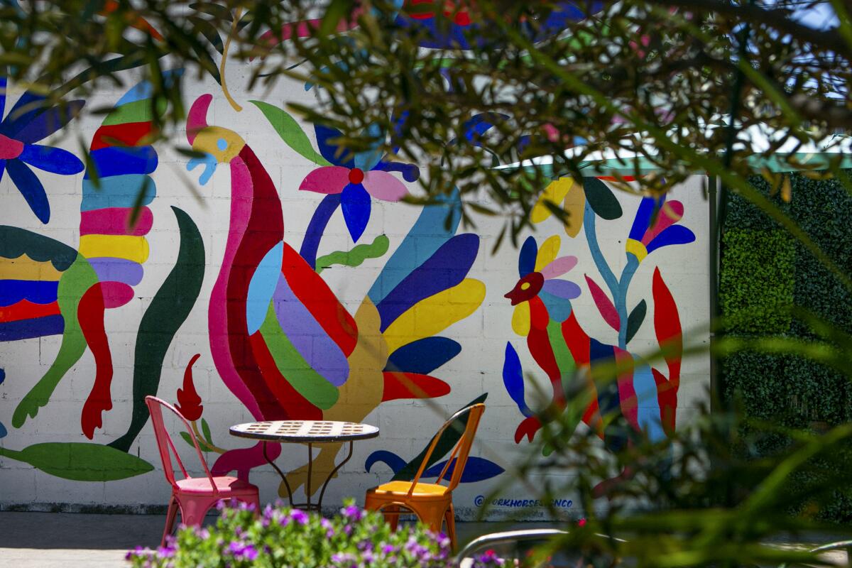 A table and chairs on a patio with a colorful mural of a rooster and other animals.